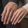 Load image into Gallery viewer, A gold plated floral spinner ring is worn on a finger, highlighting the raised botanical relief, symbolic flower pattern, and meaningful meditation ring style in a refined close-up lifestyle shot.
