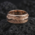 Load image into Gallery viewer, The rose gold plated art history ring is arranged on black volcanic rock, emphasizing the symbolic hands, textured background, rounded edges, and refined spinning band construction in a detailed macro image.
