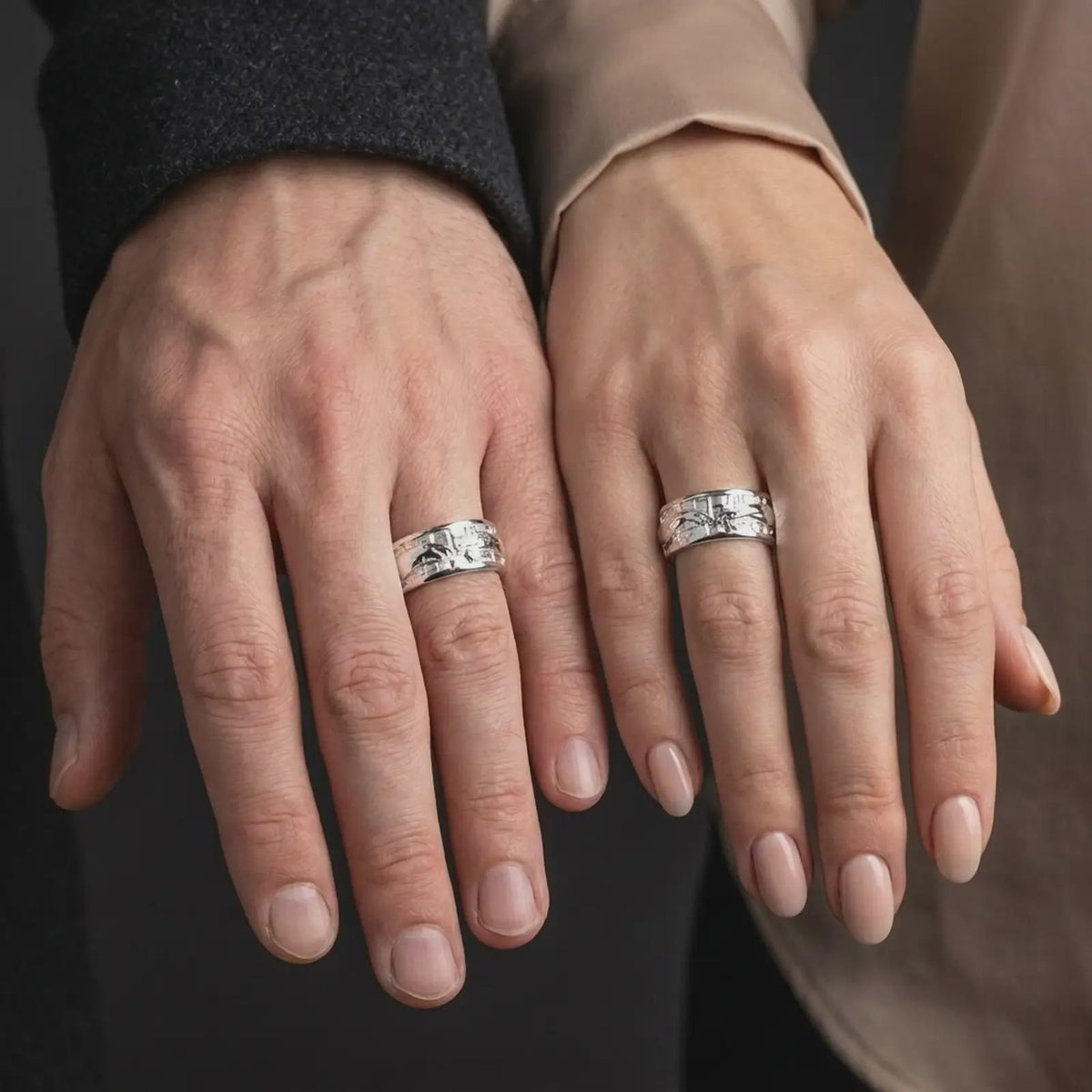 The polished silver reaching hands wedding band is worn on a finger, showing the Renaissance-inspired motif and comfortable unisex spinner ring profile in a premium lifestyle photograph.