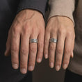 Load image into Gallery viewer, An oxidized Aztec spinner ring is worn on a finger, displaying the dark recessed pattern work, engraved panel details, and bold sterling silver band in a close-up lifestyle shot.
