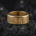 Load image into Gallery viewer, A gold plated Aztec spinner band rests on rugged volcanic rock, featuring detailed geometric pattern panels and an engravable wide ring structure in a luxury macro studio close-up.
