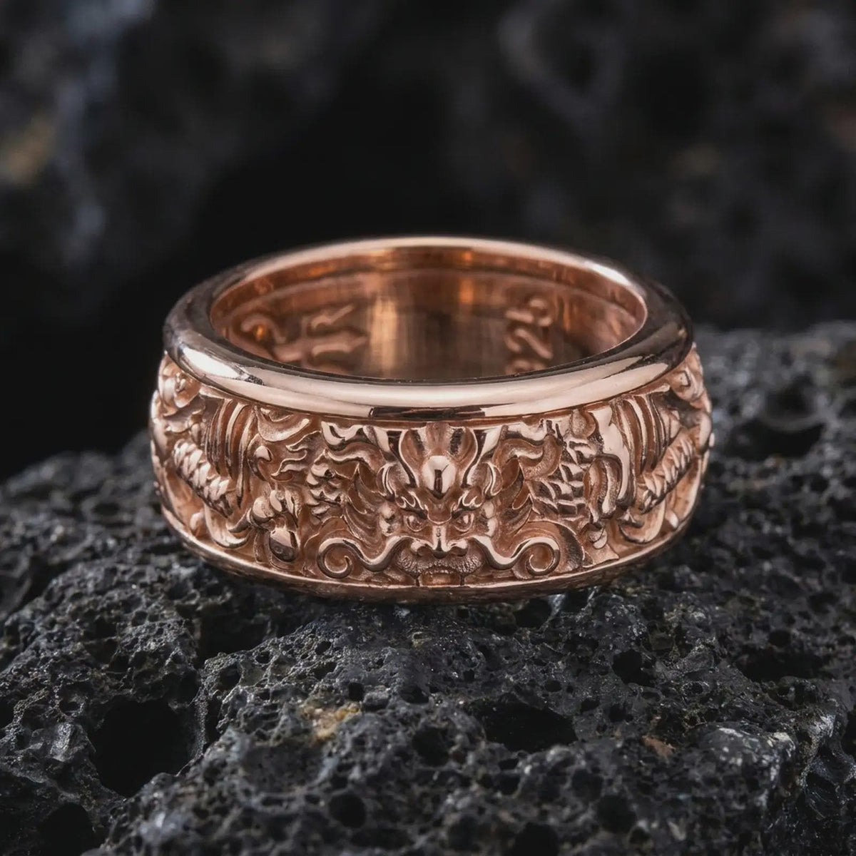 The rose gold plated serpent dragon spinner ring is arranged on black volcanic rock, emphasizing the mystical dragon relief, rich carved texture, and elegant fidget band design in a detailed macro image.