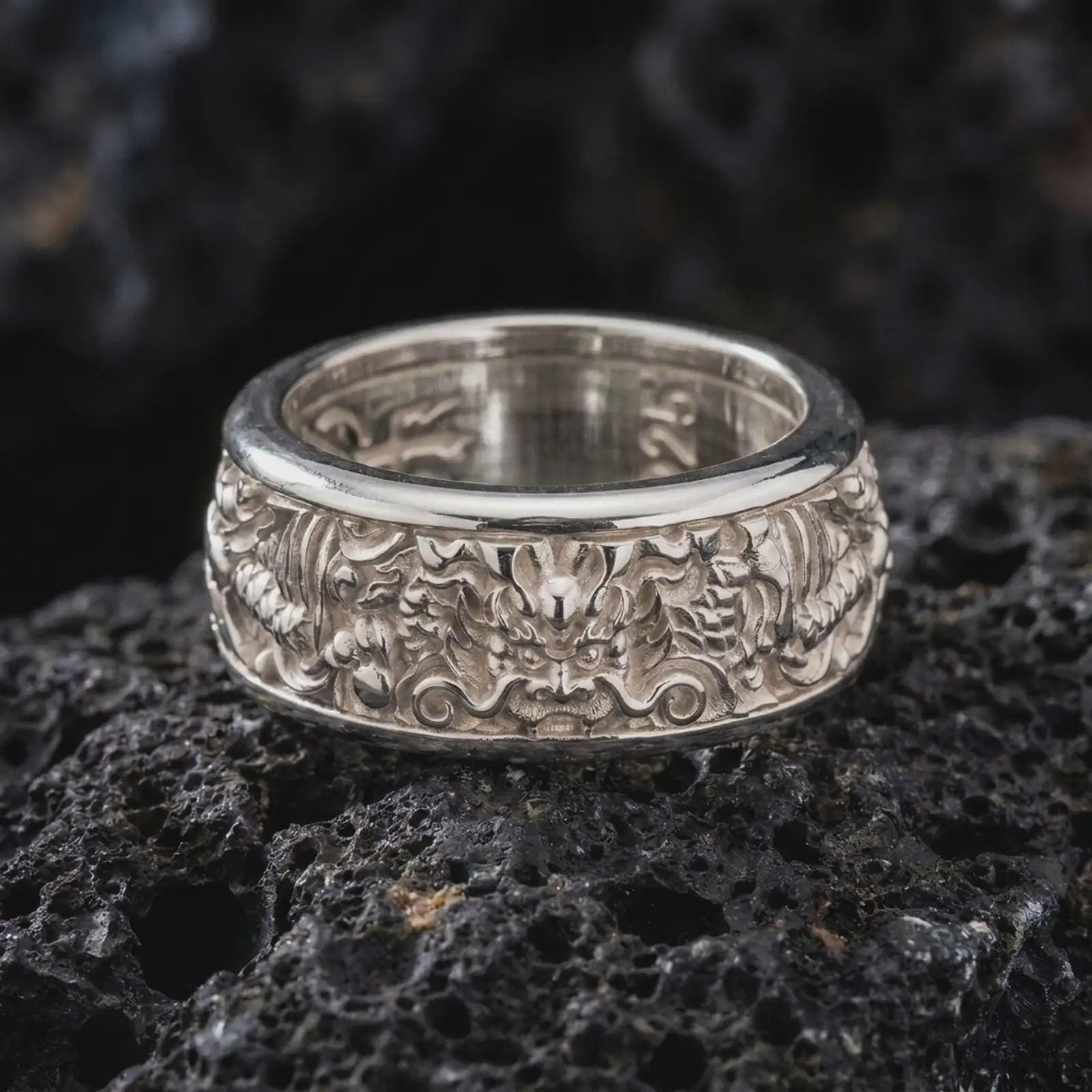 The polished silver dragon spinner ring is displayed on textured black volcanic rock, highlighting the intricate Asian serpent design, sculpted details, and smooth spinning band profile in a premium macro photograph.