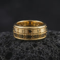 Load image into Gallery viewer, A gold plated geometric spinner ring sits on textured volcanic rock, showcasing the bold plate motif, structured fidget band design, and luxurious metallic finish in a premium macro studio image.
