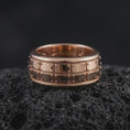 Load image into Gallery viewer, A rose gold plated plate pattern spinner ring is arranged on dark volcanic rock, featuring the segmented geometric surface, rotating band profile, and warm elegant finish in a close-up jewelry photograph.
