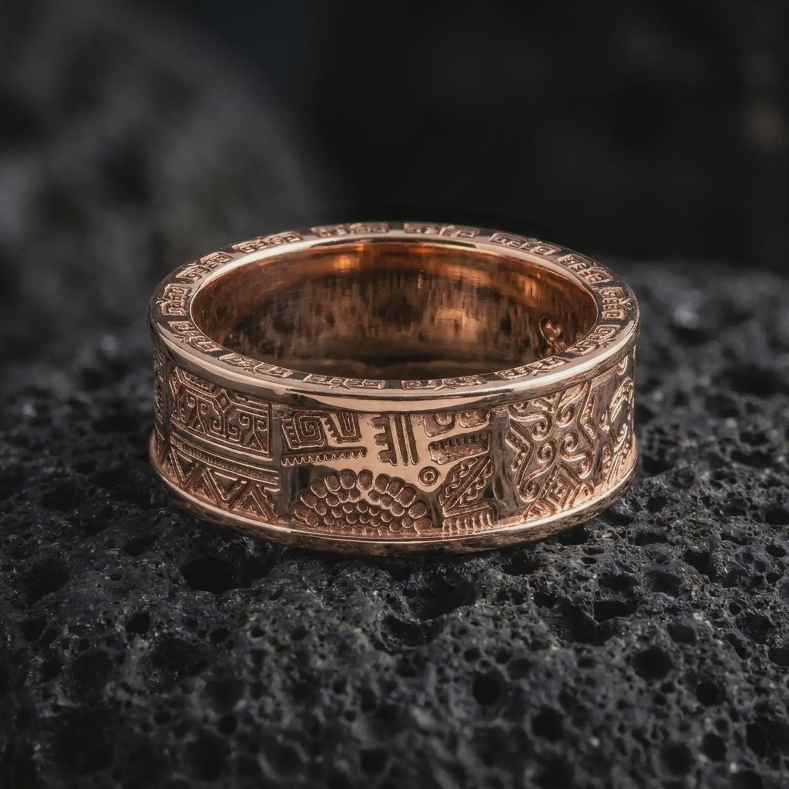 The rose gold plated geometric spinner ring is arranged on black volcanic rock, emphasizing its tribal-inspired pattern, engraved border details, and refined rotating band construction in a detailed macro image.