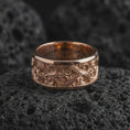 Load image into Gallery viewer, The rose gold plated scrollwork wedding band is arranged on black volcanic rock, emphasizing its flowing ornamental relief, vintage-inspired texture, and refined unisex spinner design in a detailed macro image.
