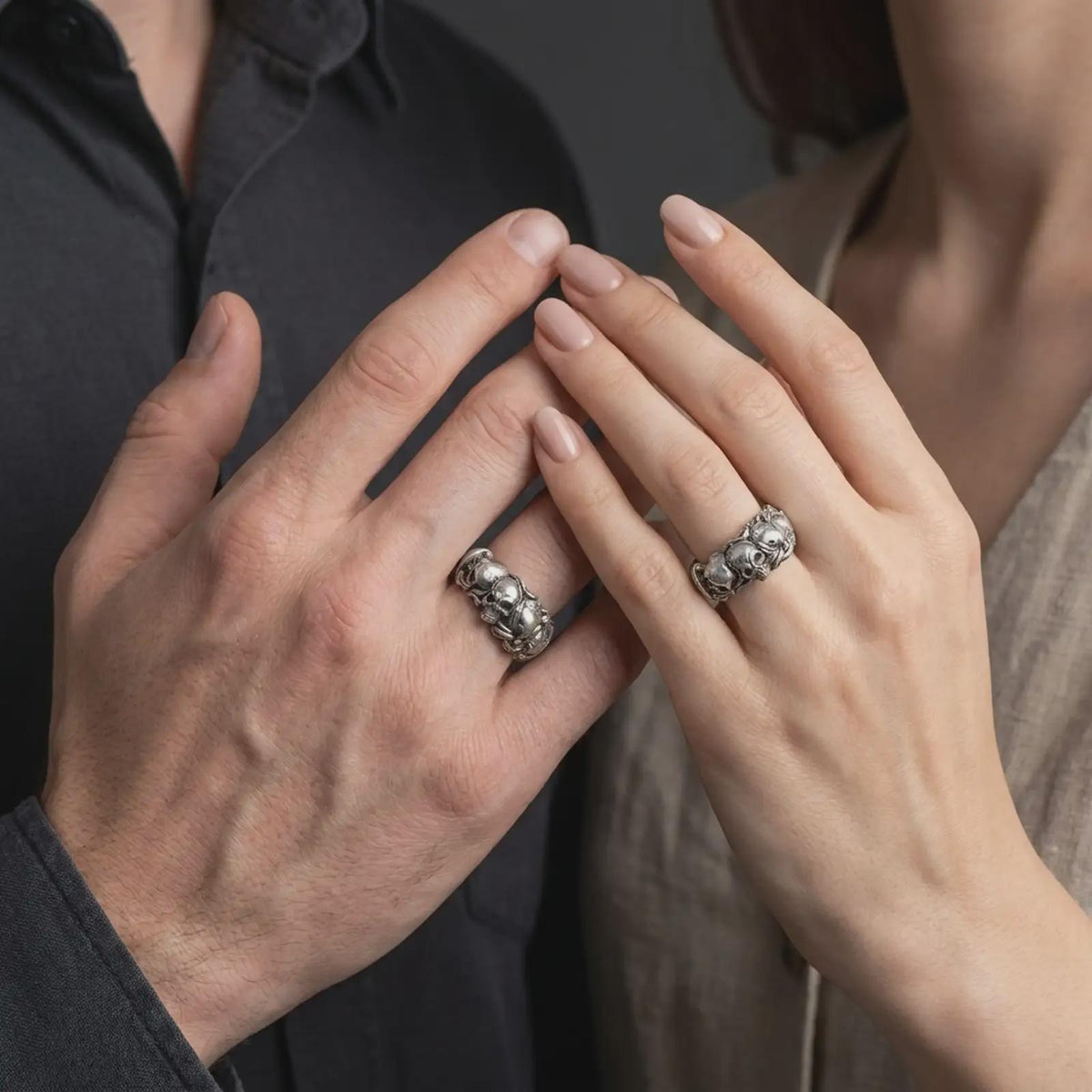 An oxidized sterling silver skull ring is worn on a finger, displaying the raised skull, surrounding roses and leaves, dark recessed detailing, and substantial gothic band profile in a close-up lifestyle photograph.