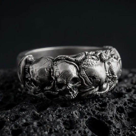 An oxidized sterling silver skull ring rests on dark volcanic rock, featuring a detailed raised skull surrounded by sculpted roses, leaves, and gothic floral elements in a dramatic macro studio close-up.