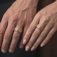 Load image into Gallery viewer, The rose gold plated fleur-de-lis spinner ring is worn on a finger, showcasing the continuous Baroque scroll pattern, textured background, rounded edges, and elegant vintage-inspired jewelry design.
