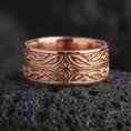 Load image into Gallery viewer, The rose gold plated Elven knotwork ring is arranged on black volcanic rock, emphasizing its mystical star centerpiece, continuous interwoven pattern, and refined fantasy-inspired band profile in a detailed macro image.
