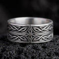 Load image into Gallery viewer, An oxidized sterling silver Elven Star ring rests on dark volcanic rock, featuring a geometric central star, flowing interwoven knotwork, and a dark recessed wide band in a macro studio close-up.
