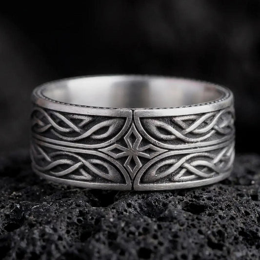 An oxidized sterling silver Elven Star ring rests on dark volcanic rock, featuring a geometric central star, flowing interwoven knotwork, and a dark recessed wide band in a macro studio close-up.