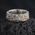 Load image into Gallery viewer, The polished silver mythical dragon ring is displayed on textured black volcanic rock, highlighting the raised dragon face, flowing ornamental details, sculpted scales, and substantial wide band profile in a premium macro photograph.
