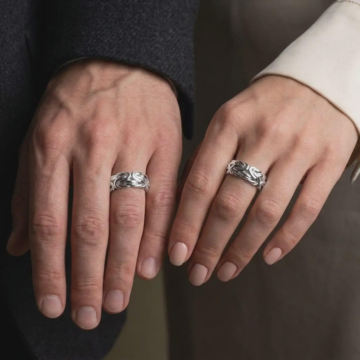The polished silver Byzantine chain band is worn naturally on a finger, showing the interlocking link pattern, smooth silver finish, and substantial everyday ring design in a premium lifestyle photograph.