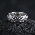Load image into Gallery viewer, The polished silver Byzantine chain ring is displayed on textured black volcanic rock, highlighting the dimensional woven links, smooth interior, and bold handcrafted band structure in a premium macro photograph.
