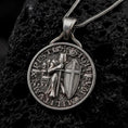 Load image into Gallery viewer, An oxidized sterling silver Templar Knight pendant rests on dark volcanic rock, featuring an armored medieval warrior with a sword, cross shield, castle backdrop, and detailed round medallion border in a macro studio close-up.
