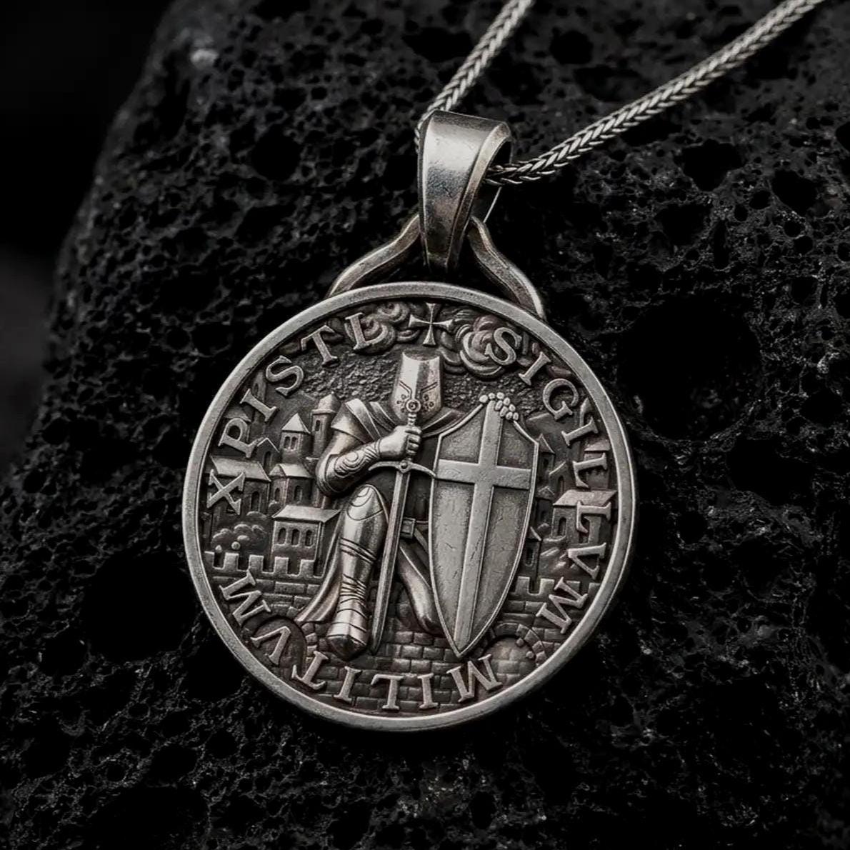 An oxidized sterling silver Templar Knight pendant rests on dark volcanic rock, featuring an armored medieval warrior with a sword, cross shield, castle backdrop, and detailed round medallion border in a macro studio close-up.