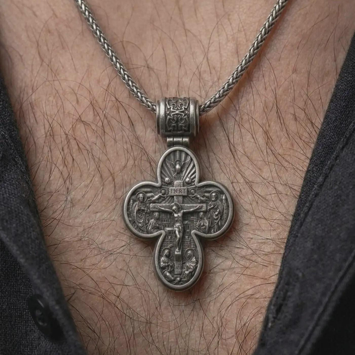 An oxidized sterling silver Saint Michael cross pendant is worn on the neck, displaying the double sided Christian design, protective symbolism, and detailed sculptural cross form in a close-up lifestyle photograph.