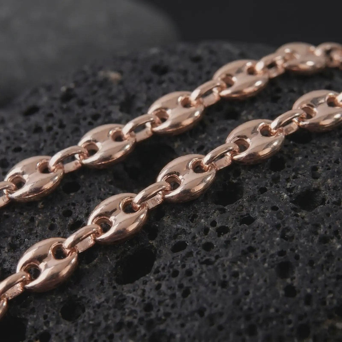 The rose gold plated 11mm Mariner necklace is arranged on black volcanic rock, emphasizing its broad oval links, central bars, smooth dimensional surfaces, and bold nautical-inspired chain profile in a detailed macro image.
