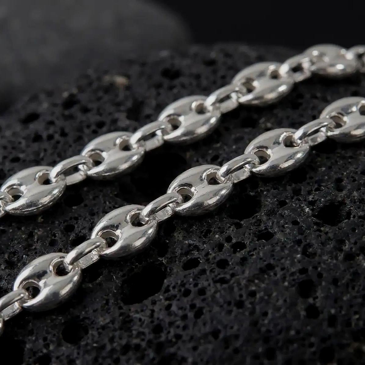 The polished silver 11mm Mariner chain necklace is displayed on textured black volcanic rock, highlighting the smooth puffed anchor links, reflective sterling silver surfaces, and bold wide-link construction in a premium macro photograph.