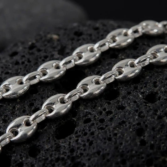 The polished silver 11mm Mariner chain necklace is displayed on textured black volcanic rock, highlighting the smooth puffed anchor links, reflective sterling silver surfaces, and bold wide-link construction in a premium macro photograph.