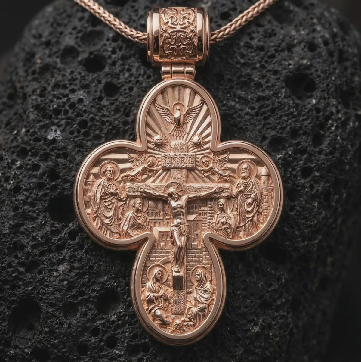 The rose gold plated archangel cross necklace is arranged on black volcanic rock, emphasizing the dimensional religious relief, decorative bail, and meaningful protection-inspired pendant design in a refined macro image.