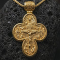 Load image into Gallery viewer, A gold plated Saint Michael protection pendant rests on rugged volcanic rock, featuring the ornate cross silhouette, devotional scene, and symbolic double sided Christian design in a luxury macro studio close-up.
