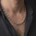 Load image into Gallery viewer, The polished silver Mariner chain is worn naturally around a man's neck, showing the smooth puffed links, classic center-bar design, and bold 11mm sterling silver profile in a premium lifestyle photograph.
