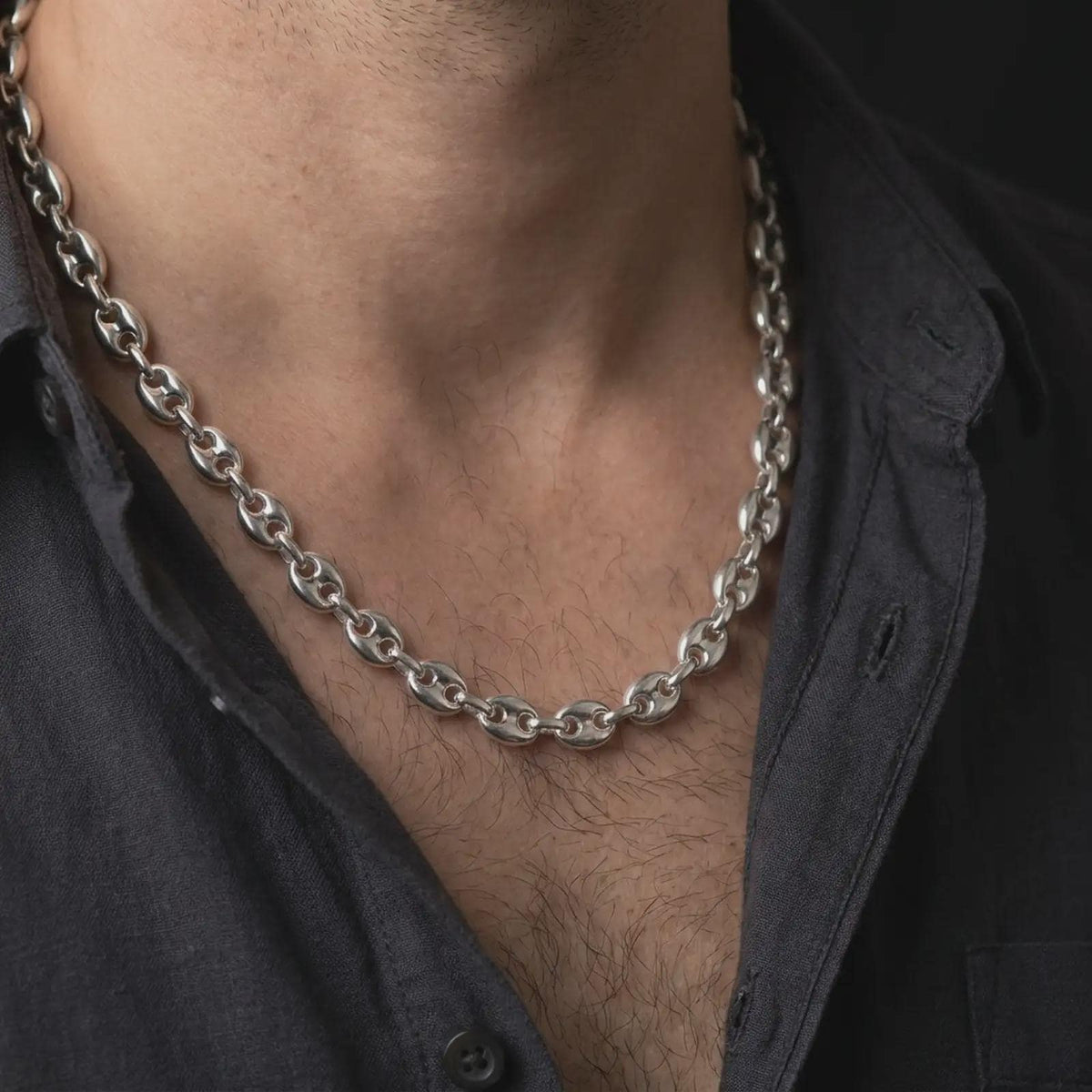 The polished silver Mariner chain is worn naturally around a man's neck, showing the smooth puffed links, classic center-bar design, and bold 11mm sterling silver profile in a premium lifestyle photograph.