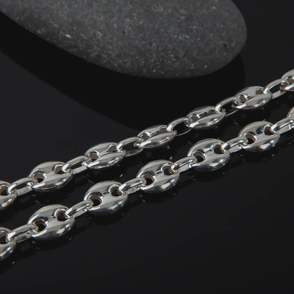 The polished silver 11mm Mariner chain necklace is displayed on textured black volcanic rock, highlighting the smooth puffed anchor links, reflective sterling silver surfaces, and bold wide-link construction in a premium macro photograph.
