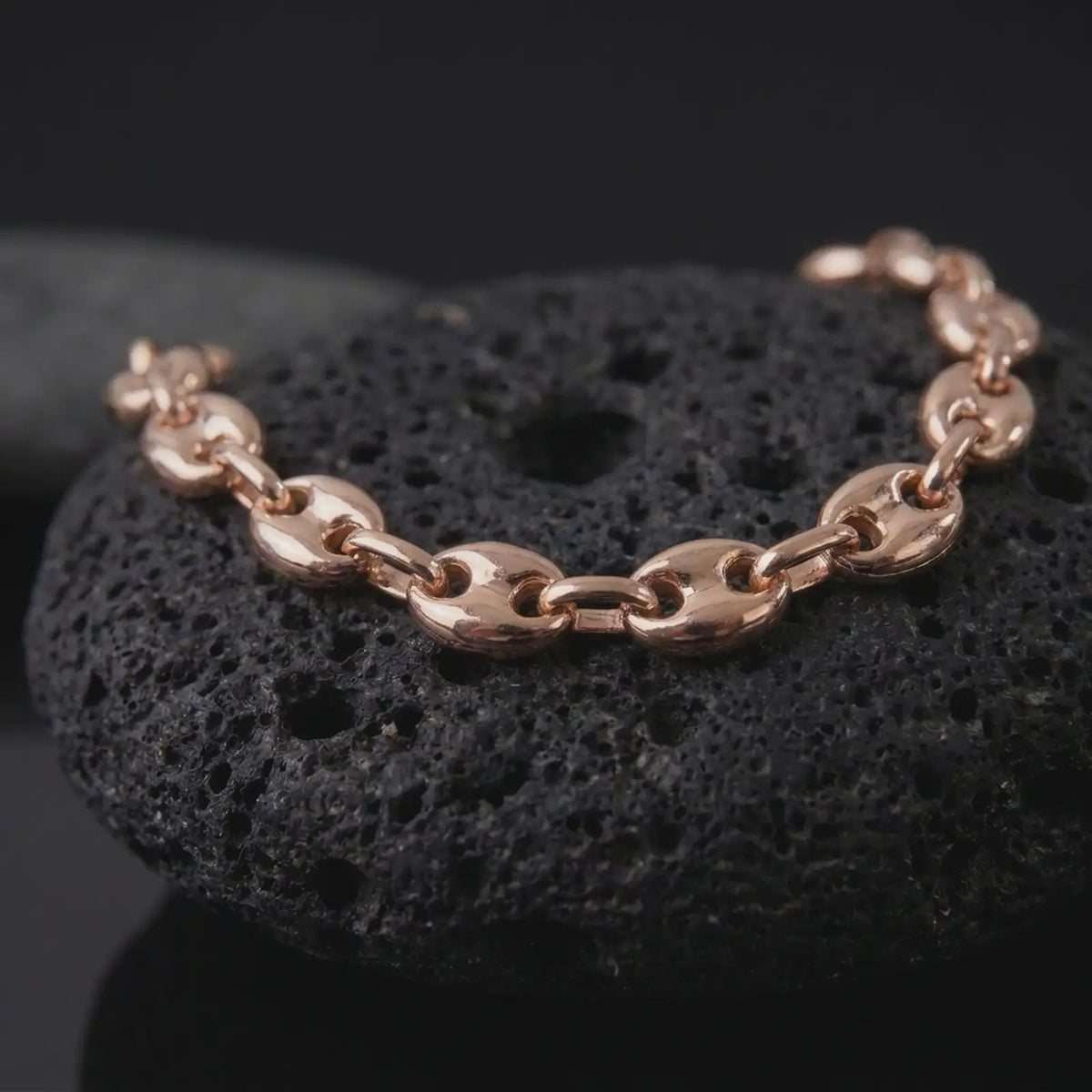 The rose gold plated Mariner bracelet is arranged on black volcanic rock, emphasizing its rounded puffed links, classic anchor chain structure, and bold 11mm statement profile in a detailed macro image.