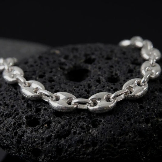 The polished silver 11mm Mariner bracelet is displayed on textured black volcanic rock, highlighting the smooth puffed anchor links, reflective surfaces, and bold wide-link construction in a premium macro photograph.