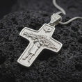Load image into Gallery viewer, The polished silver Good Shepherd cross pendant is displayed on textured black volcanic rock, highlighting the shepherd figure, flock of sheep, dove motif, raised relief, and smooth sterling silver border in a premium macro photograph.
