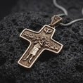 Load image into Gallery viewer, A Bronze sterling silver Pope Francis cross pendant rests on dark volcanic rock, featuring the Good Shepherd carrying a sheep, surrounding flock, dove symbol, and detailed recessed Christian imagery in a macro studio close-up.
