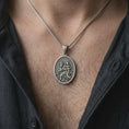 Load image into Gallery viewer, An oxidized sterling silver St. Christopher pendant is worn on the chest, displaying the oval travelers medal, raised saint and Christ Child figures, dark recessed background, and classic Catholic devotional style in a close-up lifestyle photograph.
