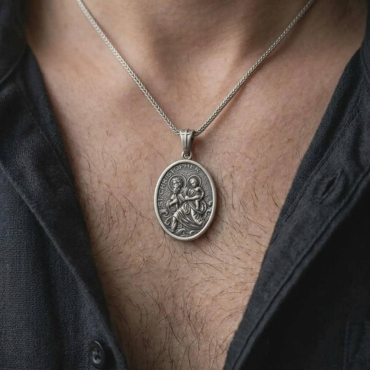 An oxidized sterling silver St. Christopher pendant is worn on the chest, displaying the oval travelers medal, raised saint and Christ Child figures, dark recessed background, and classic Catholic devotional style in a close-up lifestyle photograph.