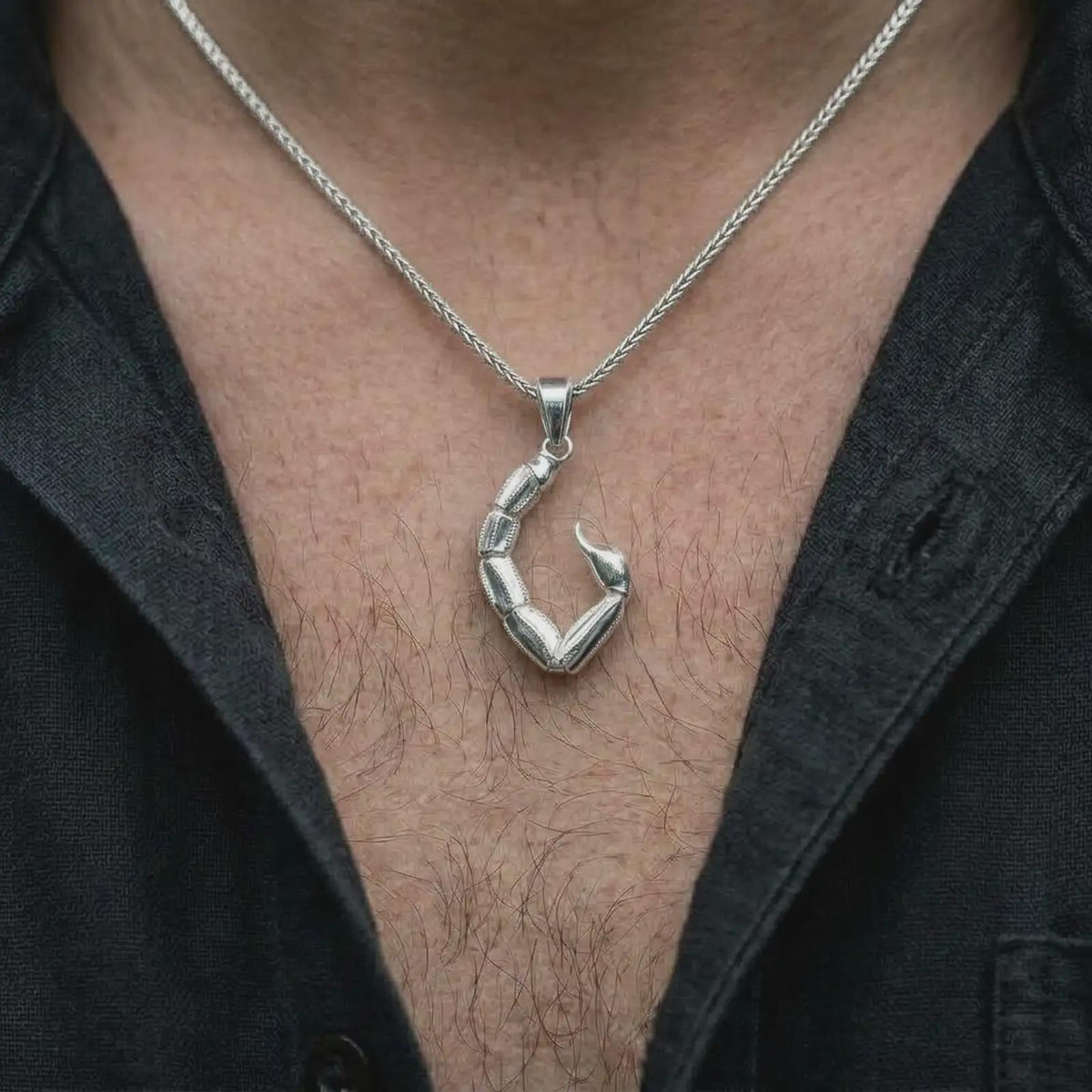 The polished silver scorpion tail necklace is worn naturally on the chest, showing the articulated segments, sleek curved silhouette, and distinctive unisex zodiac jewelry design in a premium lifestyle photograph.