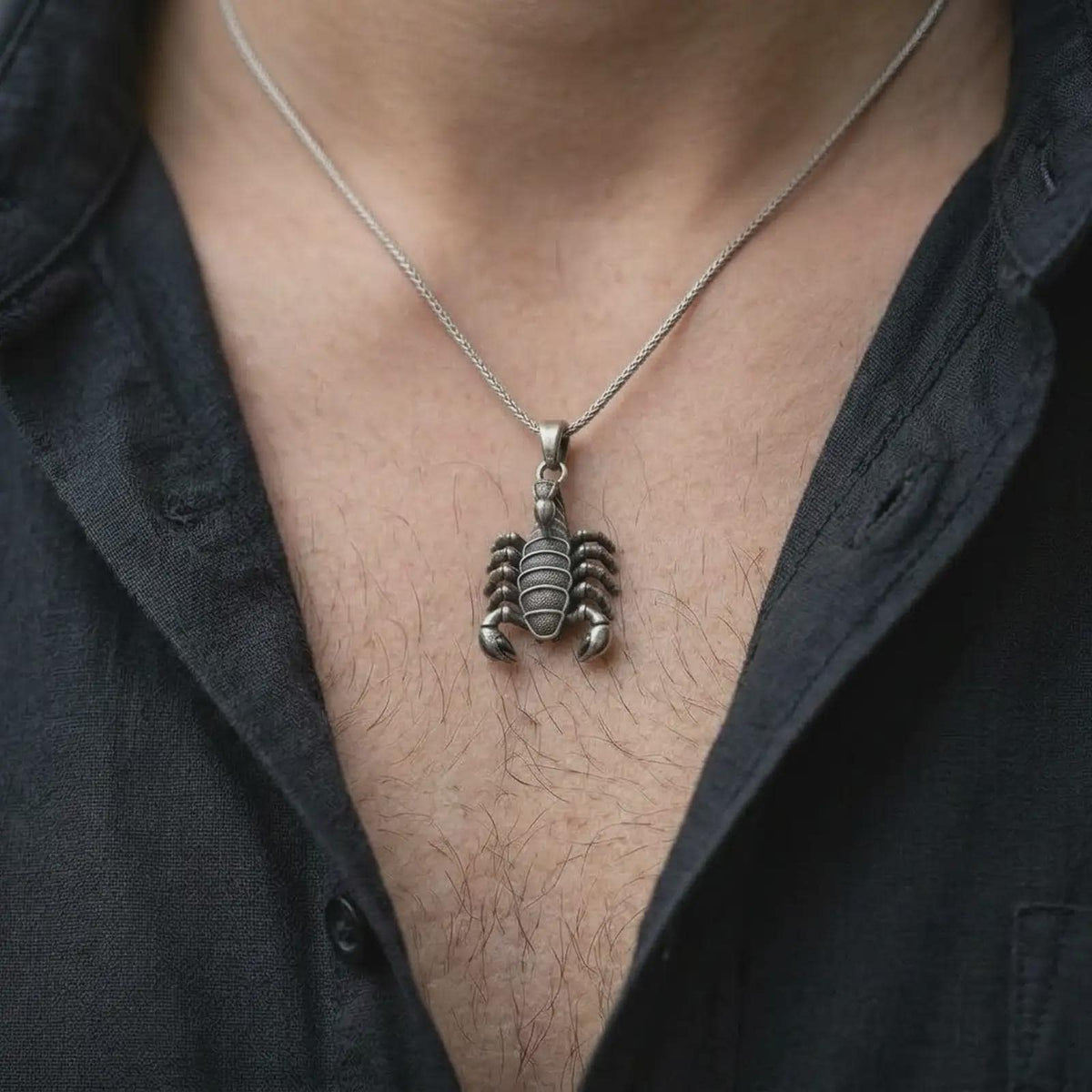 An oxidized silver Scorpio pendant is worn naturally on the chest, displaying the detailed scorpion anatomy, dark recessed textures, raised silver surfaces, and bold animal totem profile in a close-up lifestyle image.