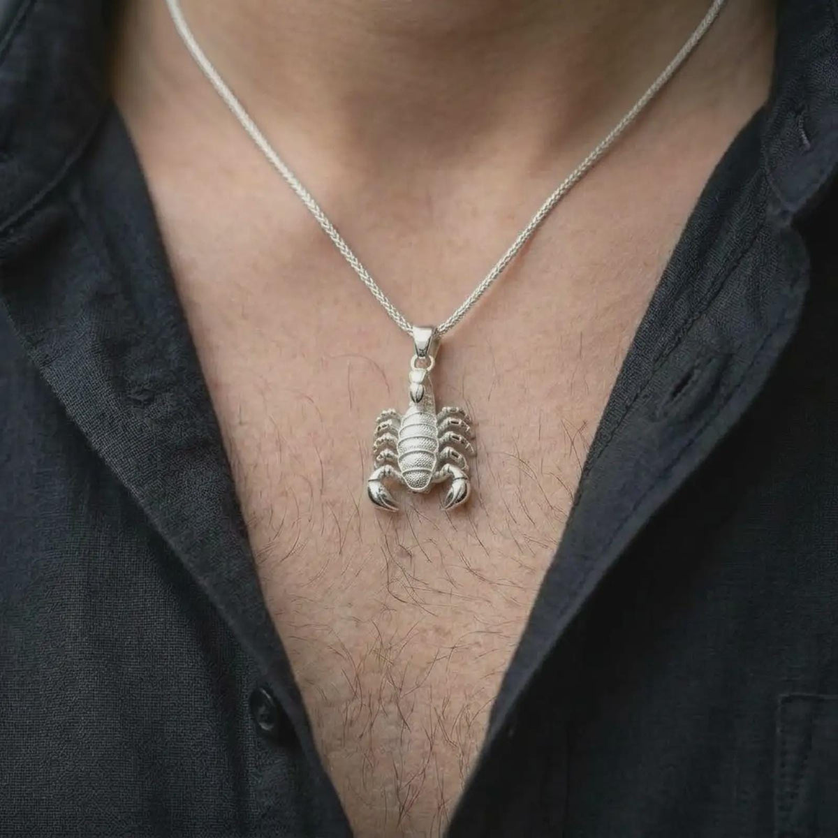An polished silver Scorpio pendant is worn naturally on the chest, displaying the detailed scorpion anatomy, and bold animal totem profile in a close-up lifestyle image.