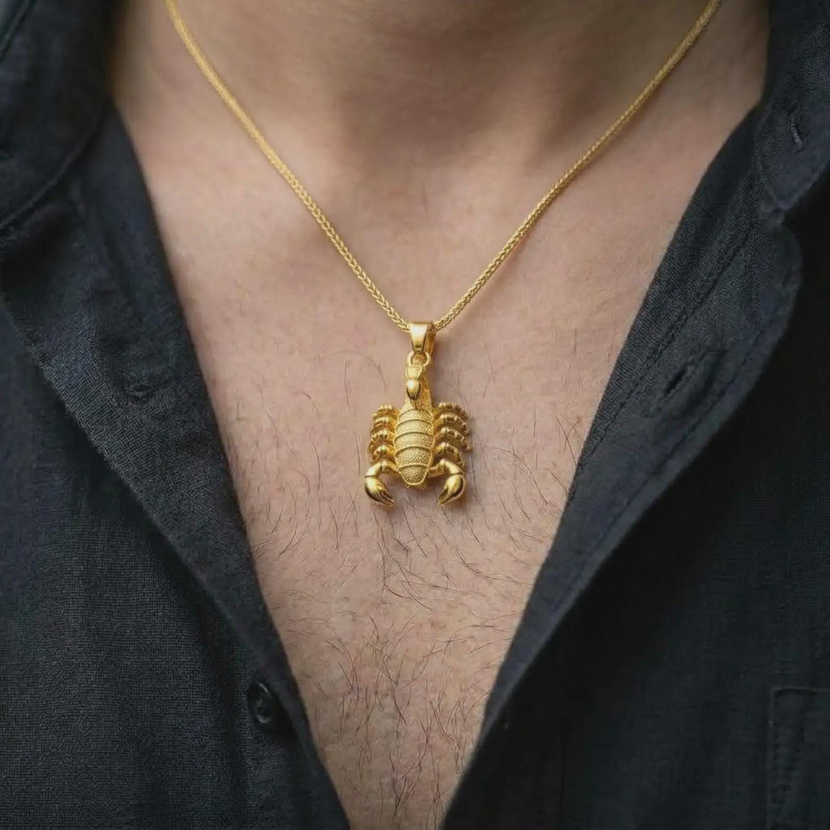 A gold plated scorpion necklace is worn on the chest, highlighting the segmented body, prominent pincers, curved tail, and distinctive Scorpio zodiac jewelry design in a refined lifestyle photograph.