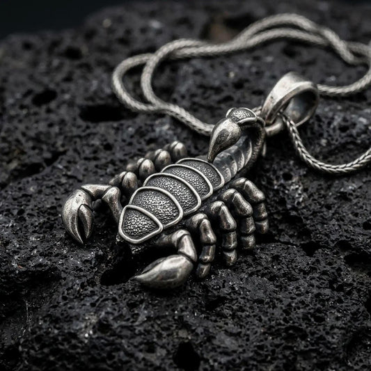 An oxidized sterling silver scorpion pendant rests on dark volcanic rock, featuring detailed claws, segmented legs, textured body armor, curved tail, and pointed stinger in a dramatic macro studio close-up.