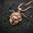 Load image into Gallery viewer, The rose gold plated insect necklace is arranged on black volcanic rock, emphasizing the ant-inspired head, textured eyes, curved antennae, dimensional facial structure, and polished statement pendant finish.

