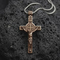 Load image into Gallery viewer, An bronze sterling silver Saint Benedict crucifix rests on dark volcanic rock, featuring the sculpted Jesus figure, INRI inscription, central Benedict medal, and textured Catholic cross details.
