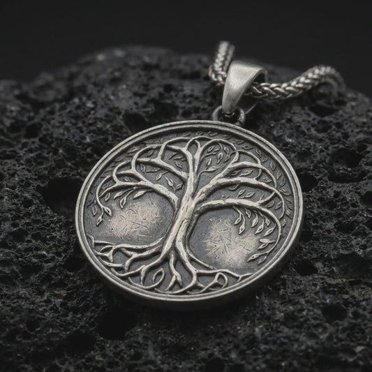 An oxidized sterling silver Tree of Life pendant rests on dark volcanic rock, featuring raised Yggdrasil branches, delicate leaves, intertwined roots, and a circular medallion with dark recessed details.