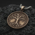 Load image into Gallery viewer, A bronze sterling silver Tree of Life pendant rests on dark volcanic rock, featuring raised Yggdrasil branches, delicate leaves, intertwined roots, and a circular medallion with dark recessed details.
