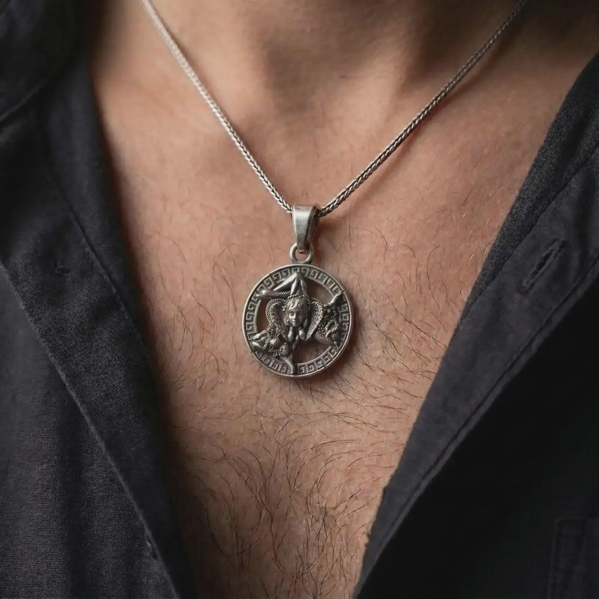 Oxidized sterling silver Trinacria necklace worn on the chest, showing the Sicilian Triskelion, Medusa centerpiece, three bent legs, and Greek key border.