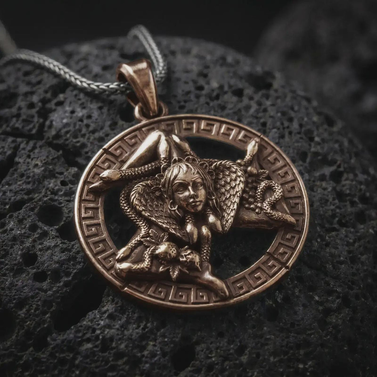 Bronze sterling silver Trinacria pendant on black volcanic rock, featuring Medusa, three bent legs, and a detailed Greek key border inspired by the traditional symbol of Sicily.