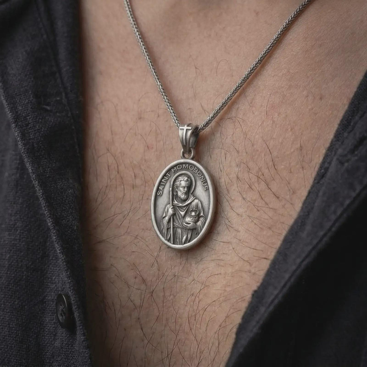 Oxidized sterling silver Saint Homobonus necklace worn on the chest, showing the detailed Catholic saint medal, halo, staff, and SAINT HOMOBONUS inscription.