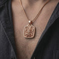 Load image into Gallery viewer, Rose gold plated Tlaloc pendant worn on the chest, showcasing the Mexica rain deity, ringed eyes, prominent fangs, and intricate ceremonial geometric details.
